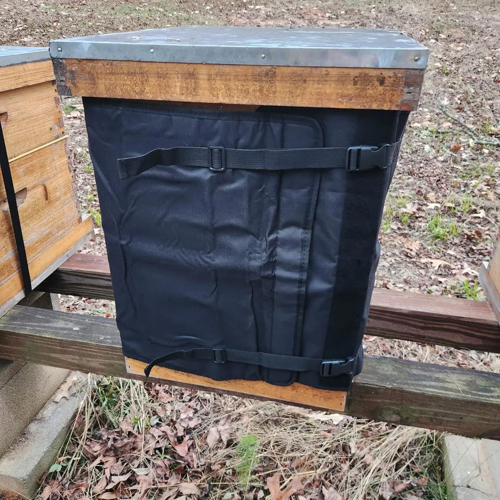 Owner-supplied Bee WinterGuard wrap installed on a wooden hive outdoors with buckle straps and metal-covered lid.